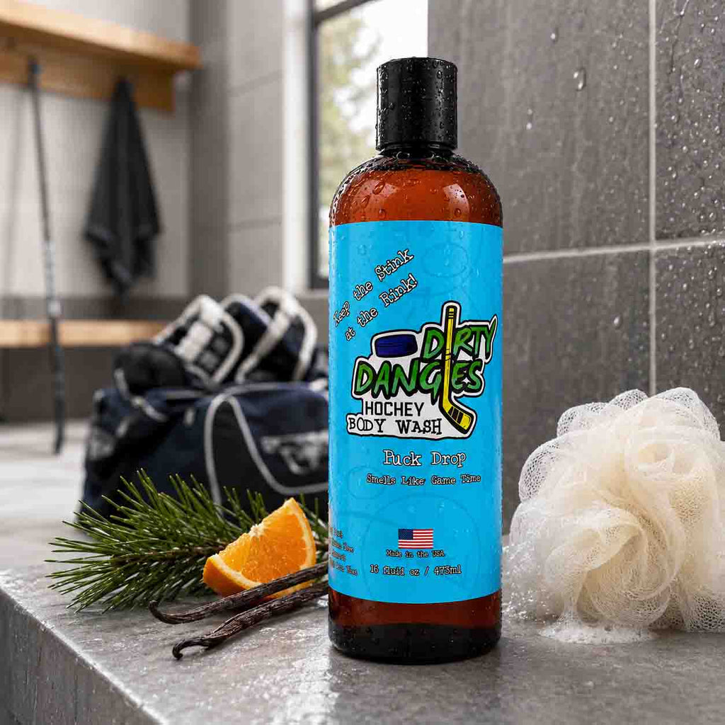 Puck Drop Dirty Dangles hockey body wash on a locker room bench with pine needles, orange slices, vanilla beans and a white loofah.
