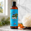 A bottle of Dirty Dangles Hockey Body Wash in puck drop scent, featuring a bright blue label and black cap, set on a marble countertop with a loofah, orange peel, pine needles and vanilla beans in a bathroom setting.