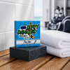 puck drop pin, orange and vanilla scented hockey soap bar on a bench in a locker room with a white towel and hockey gear