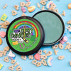 A tin of Dirty Dangles Hockey Wax Puck Luck St Patrick's Day scent on a blue background with lucky breakfast cereal