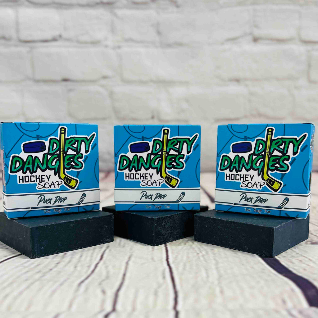 3 bars of dirty dangles puck drop scent soap against a wood and brick background. Dirty Dangles hockey soap.