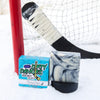 A white and black soap bar sits in the snow with a hockey goal, hockey puck and a hockey stick. Sneaky Dekes