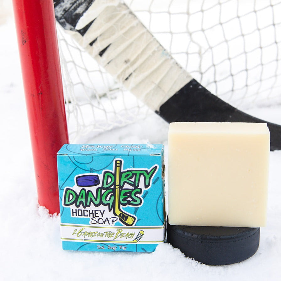 A yellow soap bar sits in the snow with a hockey goal, hockey puck and a hockey stick. 2 games on the beach