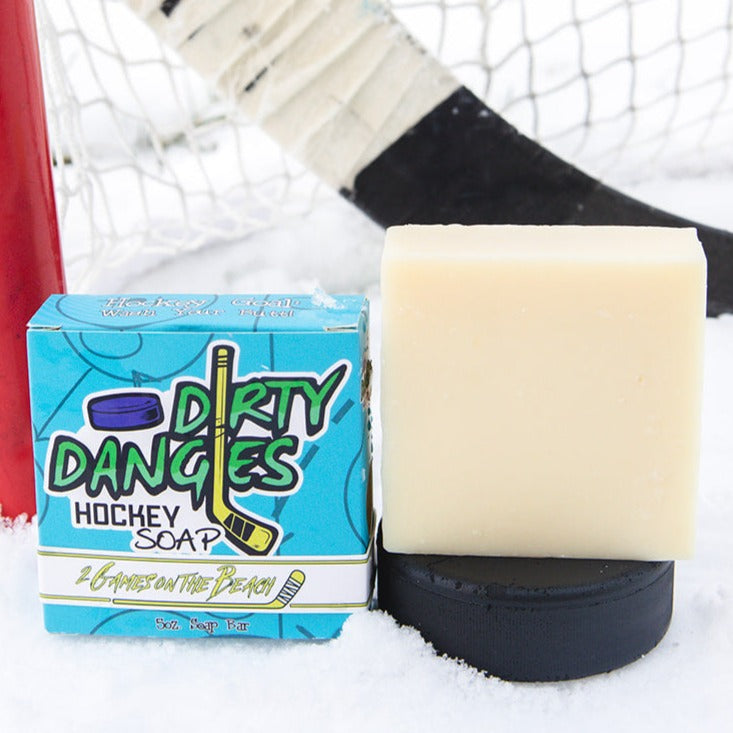 A yellow soap bar sits in the snow with a hockey goal, hockey puck and a hockey stick. 2 games on the beach scent