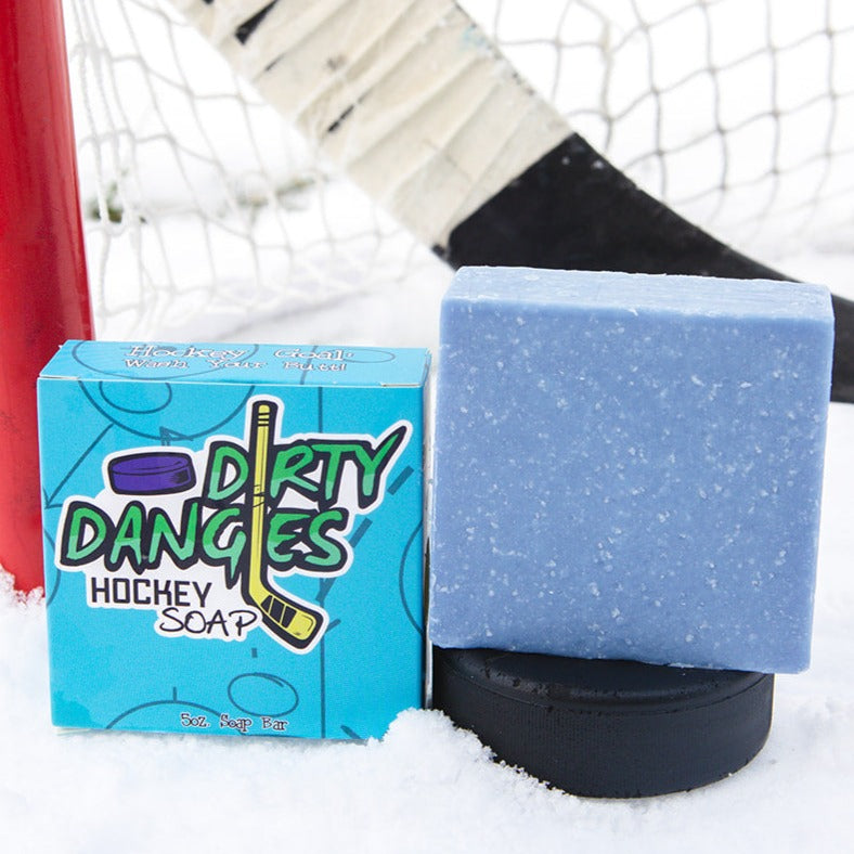 A Blue soap bar sits in the snow with a hockey goal, hockey puck and a hockey stick. The Michiganscent